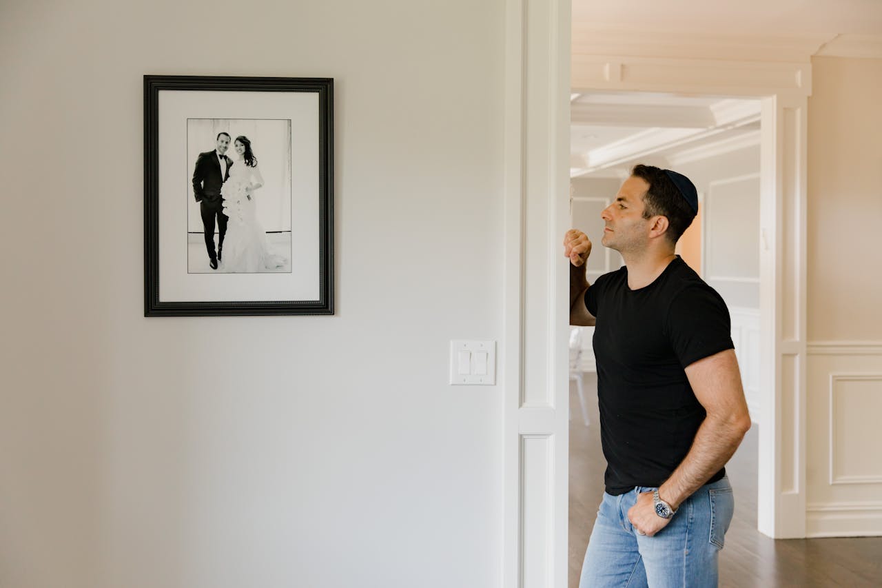 Man in black shirt admires a wedding photograph on a white wall in a contemporary home setting.