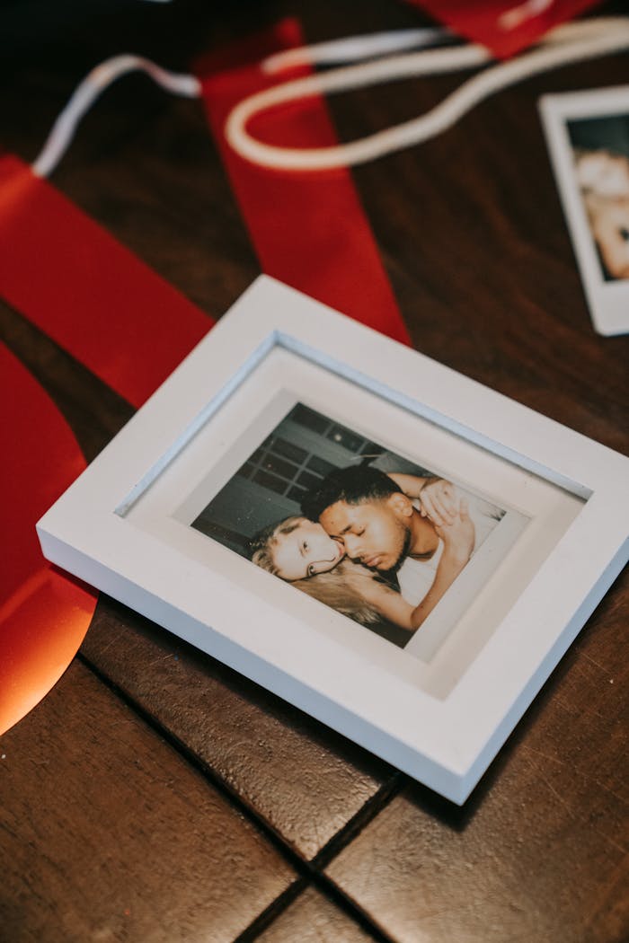 Offerings Close-up of a framed polaroid of a couple placed on a wooden table, surrounded by red ribbons.